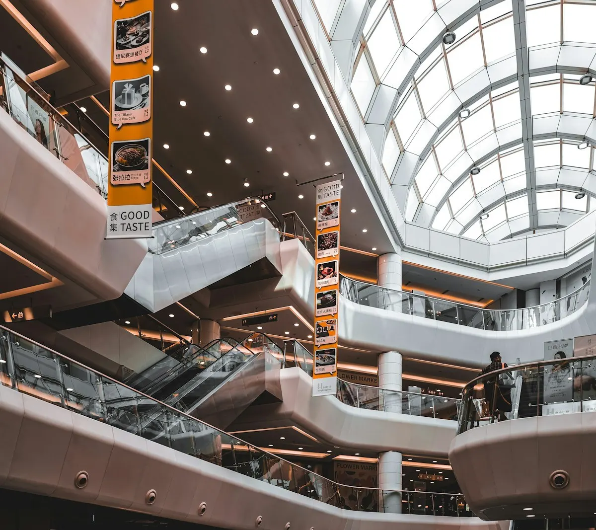 Interior de un centro comercial con escaleras mecánicas y locales bajo un techo de vidrio